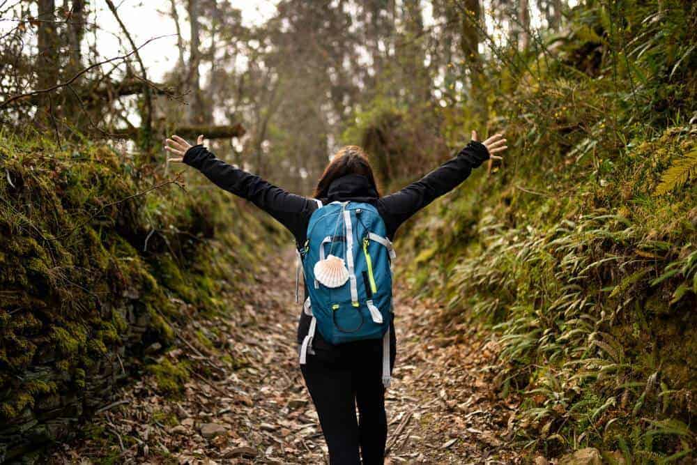 happy pilgrim young woman on the train path road walking backpack