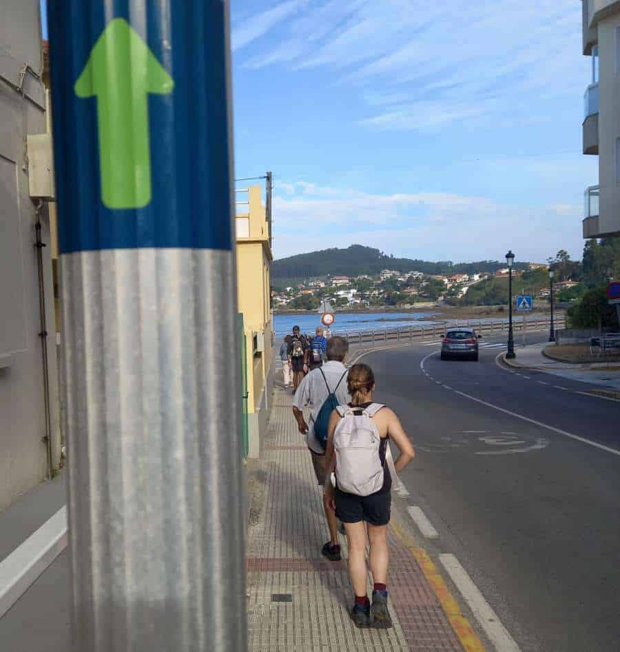 a picture of a group of pilgrims walking along the road in a town on the Camino