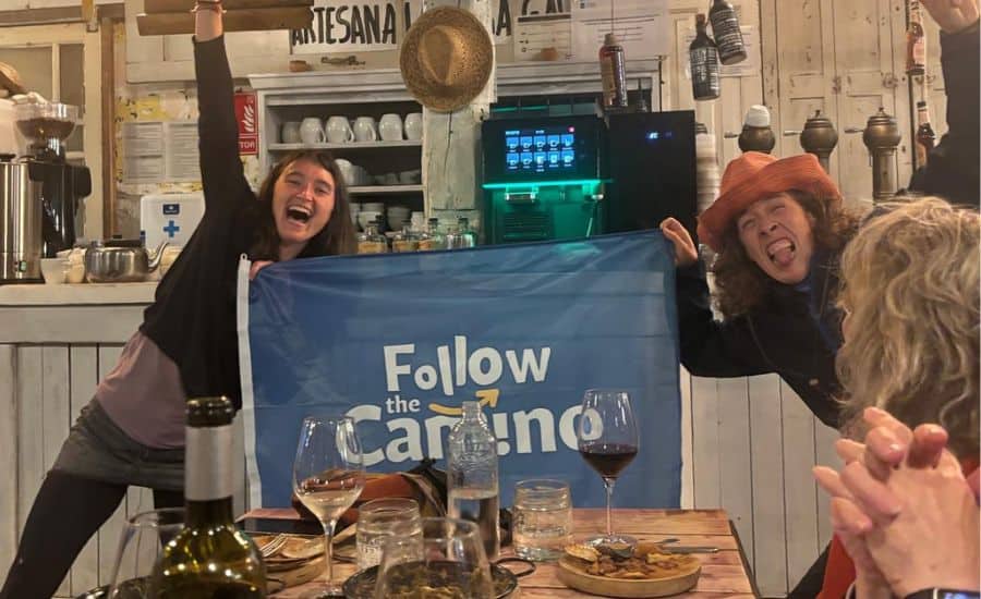 Group of happy women holding a "Follow the Camino" banner at a social gathering.